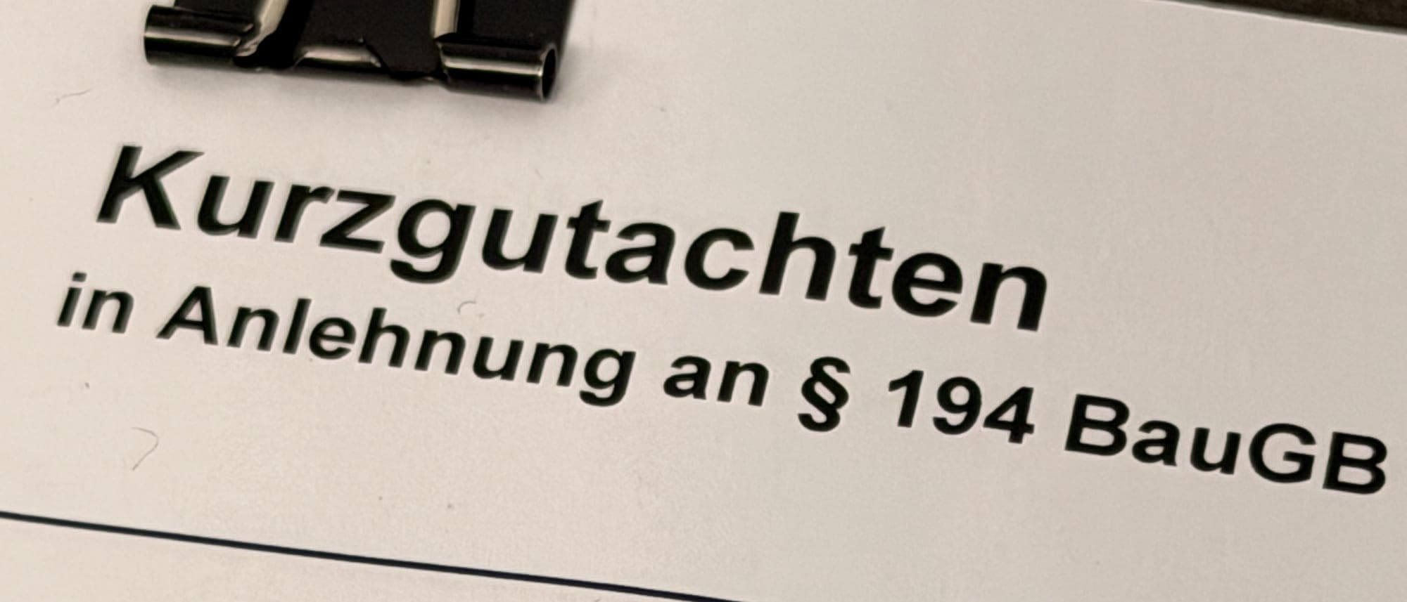 Deckblatt eines Kurzgutachtens in Anlehnung an § 194 BauGB, mit Aktenklammer auf dem Schreibtisch