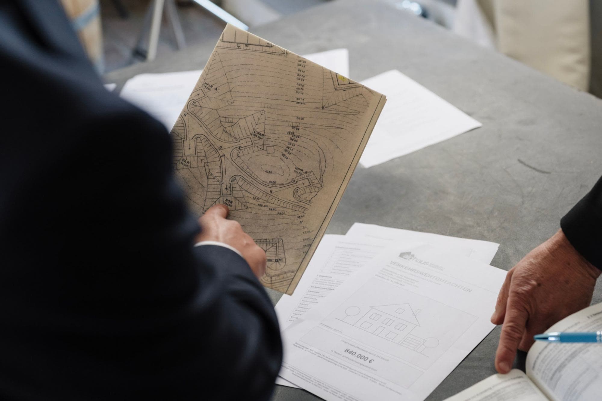 Planprüfung: Lageplan in der Hand, darunter Gutachtenseiten (Musterexemplar) und ein Fachkommentar
