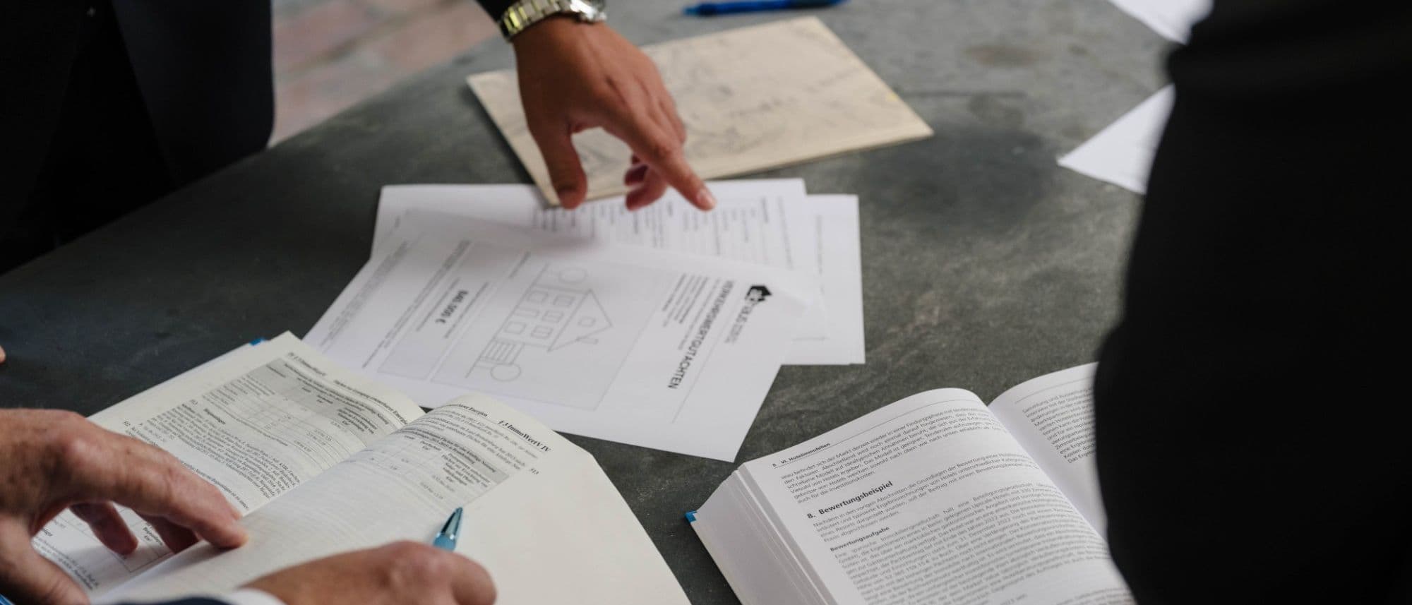 Besprechung am Arbeitstisch: Gutachtenseiten (Musterexemplar), Lageplan und aufgeschlagener Standardkommentar zur Wertermittlung