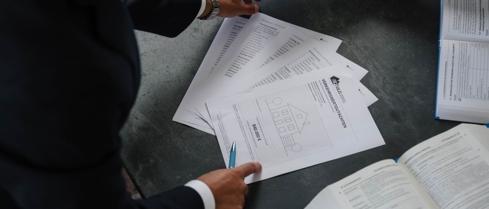 Seiten eines Verkehrswertgutachtens nach § 194 BauGB aus unserem Haus, aufgefächert auf dem Arbeitstisch — Musterexemplar mit Deckblatt, Inhaltsverzeichnis, Ergebnis, Ertragswert- und Sachwertermittlung