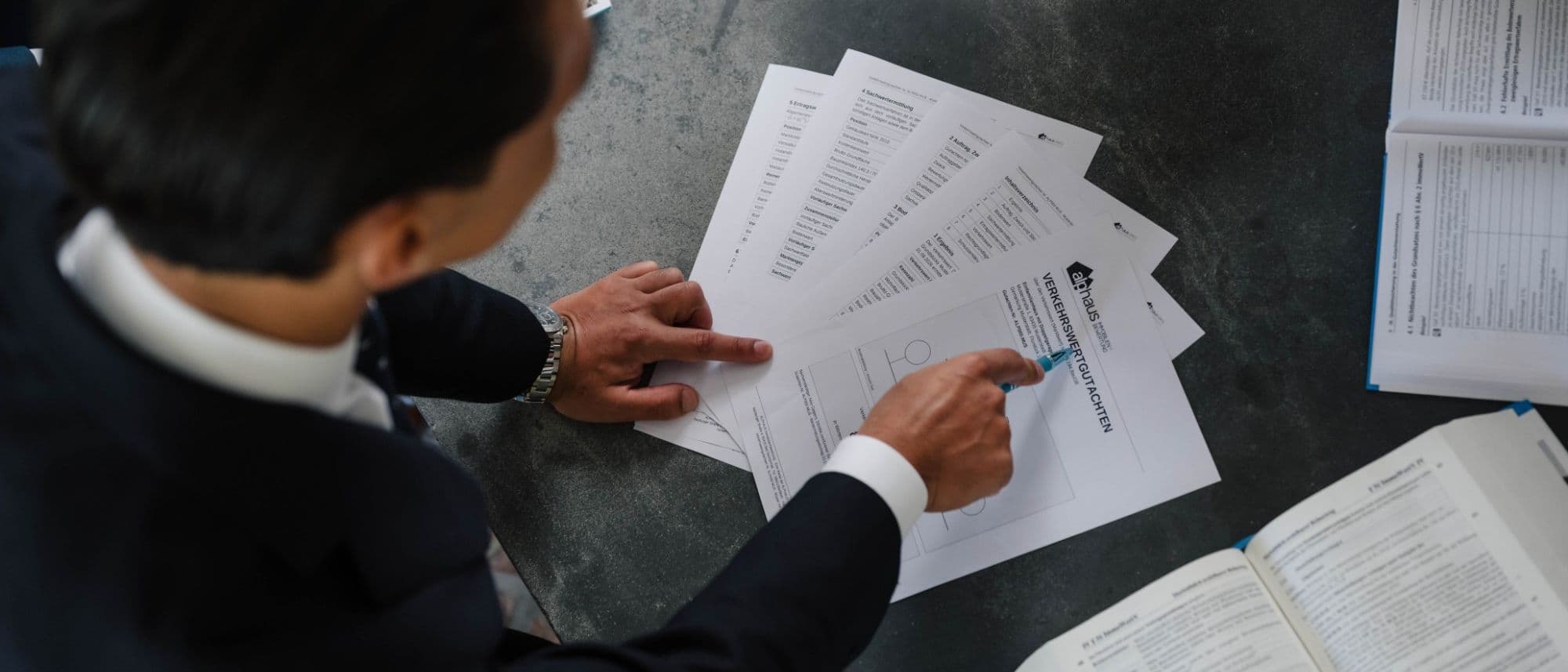 Durchsicht der Gutachtenseiten am Arbeitstisch: Deckblatt, Ergebnis und Berechnungsteile eines Musterexemplars liegen aufgefächert nebeneinander
