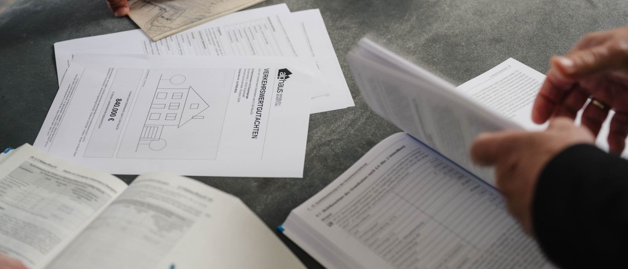 Sachverständiger schlägt im Standardkommentar zur Wertermittlung nach, daneben das Deckblatt eines Verkehrswertgutachtens (Musterexemplar) und ein Lageplan