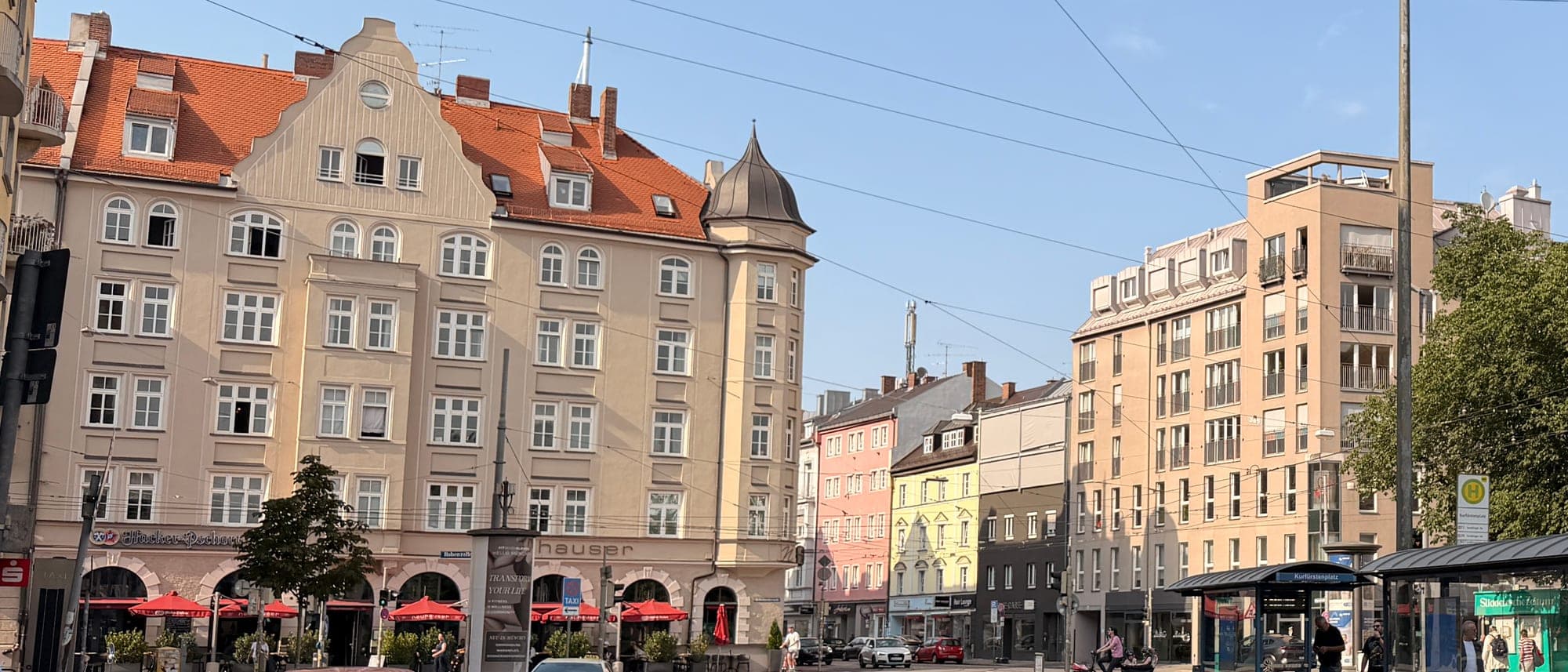 Kurfürstenplatz in München-Schwabing: Gründerzeit-Eckhaus mit Turm und Wirtshaus im Erdgeschoss, daneben Altbauzeile und moderner Wohnriegel